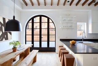 White kitchens with black countertops don’t have to give a harsh vibe. This crisp, clean, eat-in kitchen boasts high-end appliances from Viking, Bosch, Sub-Zero, and LG. An arched carriage entrance and exposed beams connect the kitchen to this home’s rich past.