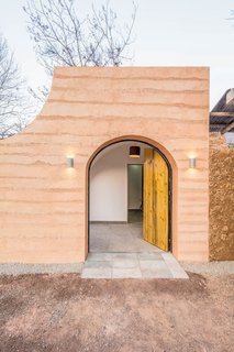 In the renovation of a traditional cave home in Weinan, China, the arched front entrance mimics the curve of the caves, and the wooden front door with contrasting black hinges swings open in two parts.