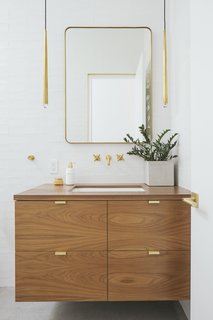 Now, the bathroom is a beautiful blend of white, wood, and brass. The Lucent mirror and Aquitaine pendant lighting in burnished brass are from RH Modern. 

