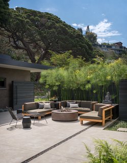 A concrete fire pit on the outdoor patio provides a place for outdoor entertaining, with ample space kept open for spontaneous dance parties. The sofa is from Henry Hall's Tru/Pure collection with fabric from Christian Liaigre and McGuire. The Tekka side table is from Christian Liaigre. An Allan Gould midcentury modern iron-and-rope lounge chair and ottoman complete the scene. 