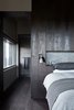 Modern home with Bedroom, Wall Lighting, Bed, and Dark Hardwood Floor. The minimalist material palette incorporates light and shadows into a tonal, textural mix. The dark flooring and paneling are both Nero Oak Volcano from Mafi. Photo 7 of Oikos at Breakneck Gorge