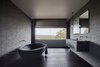 Modern home with Bath Room, Marble Counter, Porcelain Tile Wall, Freestanding Tub, Pendant Lighting, Soaking Tub, and Dark Hardwood Floor. The dramatic, handmade, black concrete soaking tub is from Boyd Alternatives, a local Victorian company that produces handmade baths. The color is an addition to the concrete mix. Photo 10 of Oikos at Breakneck Gorge