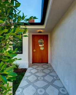 A brass-inlay terrazzo path leads to a custom-made door with a brass doorknob and a window of overlapping circles.