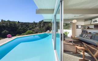 The post-and-beam guesthouse at the edge of the pool features wraparound glass windows and sliders.