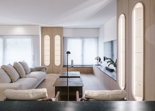 In the living room, oval-framed, oak wood display shelves and low-lying cabinetry match the large storage cabinet at the entrance. A Holden sofa by Verzelloni sits adjacent to Alison lounge chairs by Flexform. The table lamp is by Marset, and the reading lamp is by Vibia.