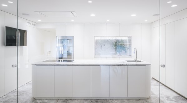 The all-white, minimalist kitchen is a transitional space between the public and private areas. A marble-topped island is oriented toward the dining room.