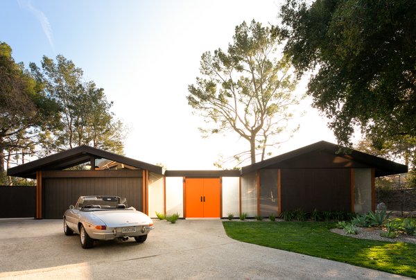 The U-shaped, one-level home is composed of two volumes connected by bright orange doors that pop against the dark wood facade.  