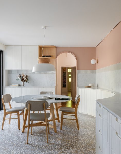 The table and chairs are pieces that the client had from before. A HAT pendant light from Luke Mills hangs over the table. The dining nook is lined with custom storage created by Carter Williamson that includes a curved cutaway to echo the round table and allow for comfortable movement. The backsplash and the countertop are both cut from elegant Cararra marble slabs.