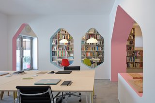 At the entrance, a meeting space can be converted into a gallery showcasing the studio’s lighting collection. Playful hexagonal windows separate the meeting area from the workspace, and a chunky pink structural arch leads to a display and storage niche.