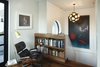 The upper landing in the White Street Residence provides a pausing point when going to and from the roof garden. A walnut bookshelf, an extension of the walnut knee wall below stores a collection of the owner's art books. The large circular window which overlooks the roof garden can be seen in the background. A vintage Grasshopper floor lamp by Greta Grossman provides reading light while relaxing in the Eames 670 lounge chair. Photo 12 of White Street Residence modern home