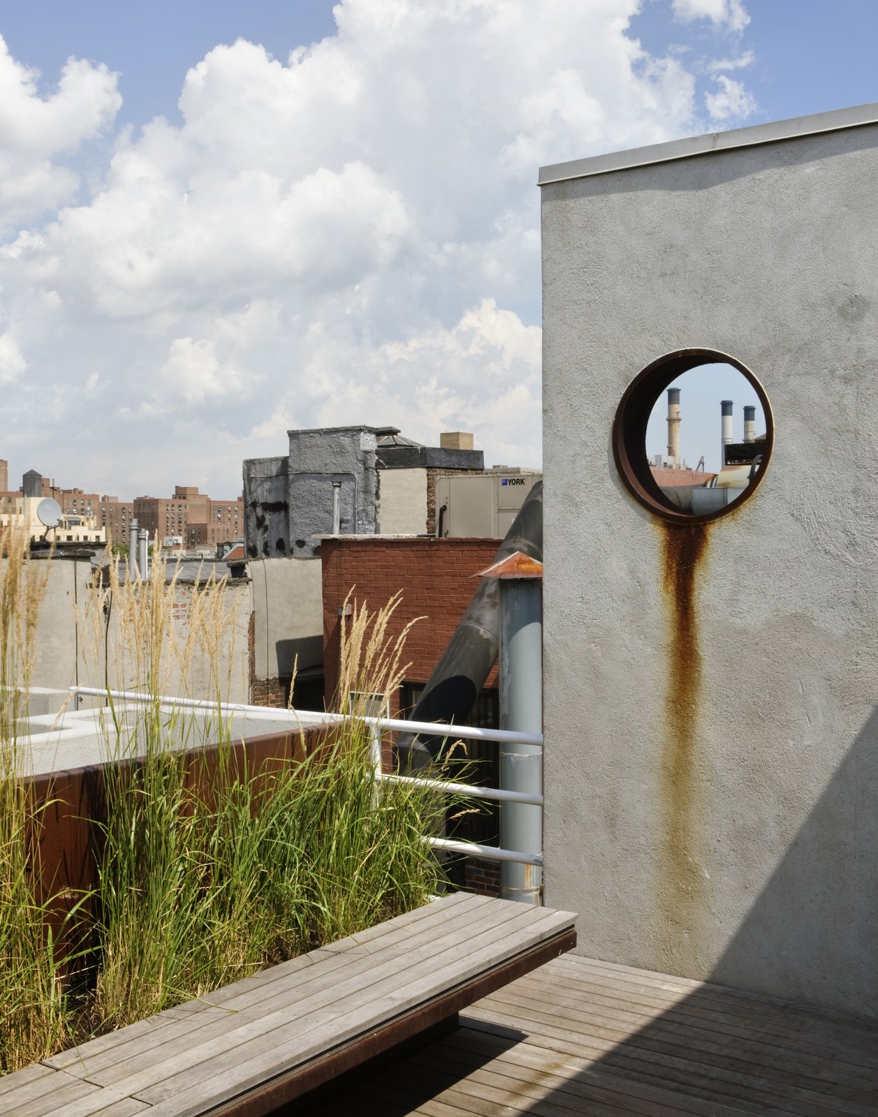 The garden is accessed from a rooftop penthouse designed by pulltab and built two years earlier.  A large diameter steel pipe was cut and placed into a new stucco wall.  This aperture frames a view to a power plant located on the Lower East Side.  The steel ring was left unpainted so it can rust and bleed down the wall.   The floating bench is made from Cor-Ten steel and teak which is left to weather a beautiful grey.