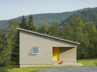 A cutaway in the structure's cubic shape forms a front porch, where a graphic yellow door welcomes visitors. The roof slopes downwards, holding more intimate spaces at its lower end.