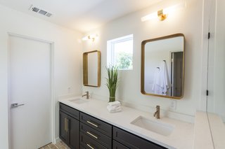 The master bathroom features brass mirrors, light fixtures, and hardware, taking visual cues from the brass accents found in the kitchen. 