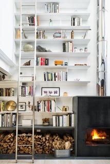 The double-height living room provided the perfect opportunity to combine the homeowners' love of art, literature, and travel, allowing them to fill the 24-foot shelves with books and collected artifacts. A wood-burning sustainable fireplace by Wittus adds a broad stroke of warmth.