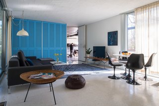 A Bertoia Bench in white oak supports the TV in the family room, while a 50th anniversary-edition Saarinen Tulip Table and Chairs provide a dark contrast to the cheery interiors. The vintage spun aluminum light fixture is also original to the house. Notice how the curtain, when open, can be neatly tucked into a nook beside the blue closets.