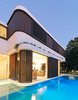 By dividing the first floor walls in three strips, the horizontality is reinforced; a lower structural spandrel below the windows, finished with an acrylic white render, a middle window strip with timber shutters and timber “log cabin” weatherboards, and an upper roof edge also finished with an acrylic render.
© Justin Alexander Photo 9 of The Pool House modern home