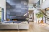 Modern home with Living Room, Pendant Lighting, Light Hardwood Floor, Sectional, Gas Burning Fireplace, and Standard Layout Fireplace. The double height hearth divides the main living spaces from the private bedrooms. Photo 10 of Wildwood