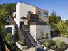 Modern home with Staircase. The simple volumes of the design and building structure are articulated by the material selections. Natural stone tile walls are both the structure and design expression of the ground floor parking area while the walls of the upper two floors feature horizontal wood planks and operable windows. The warm tones of the wood plank walls are complimented with warm white stucco plaster walls at the elevator, and dark brown/black trims on the doors and windows. Exterior railings and privacy screen walls are a mix of painted metal and wood slat. Pulling these disparate elements into a holistic design was paramount to the success of the project. Photo 3 of Modern Multi-Family Architecture