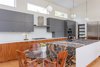 Modern home with Kitchen, Wood Cabinet, Engineered Quartz Counter, Glass Tile Backsplashe, Dishwasher, Range Hood, Refrigerator, Drop In Sink, Wall Oven, Stone Counter, Microwave, Cooktops, Light Hardwood Floor, and Pendant Lighting. The kitchen features Kendall gray upper cabinets above a continuous row of natural walnut lower cabinets topped with white quartz. The island features Sedna granite on the top and two sides. The other two sides are white quartz. Photo 11 of The Thomas Residence