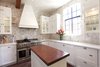 Modern home with Kitchen, Stone Counter, Brick Floor, Wood Cabinet, Marble Counter, Stone Slab Backsplashe, Recessed Lighting, Refrigerator, Drop In Sink, Range Hood, and Range. The custom chef’s kitchen showcases hand-cut marble stone walls, Italian white marble countertops, stainless steel appliances, and a professional Capital range. Photo 6 of A Charming 1920s Spanish in West Hollywood's Storied Norma Triangle
