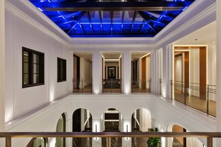 A 100-year old olive tree sits at the first floor of this atrium at the entry to a Beverly Hills mansion. On the second floor, the corridors of the second level open out to the level below, while a glass skylight above allows daylight to stream in.