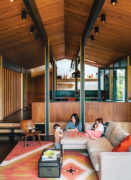 In this updated 1950s Portland home, a light gray Neo sofa by Bensen harmonizes with warm wooden walls, ceilings, and floors, as well as a red-and-mustard-yellow vintage rug.