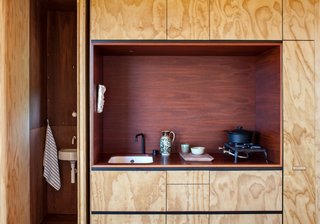 Oiled jarrah eucalyptus contrasts with a kitchen niche of reddish-brown stained plywood in this kitchen alcove in a New Zealand cabin.