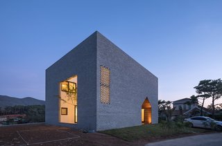 A home in South Korea designed like a large square box with the form of a small gabled house cut out to create a wide passageway.