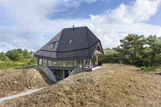 Located on the top of a sand dune, the Vlieland house is dominated by a high roof that was inspired by the De Waard Albatross tent, a popular pyramidal camping tent designed by Dutch tent makers De Waard in 1961. The ground floor—where the communal areas like the living lounge, kitchen, and covered terrace are located—are fitted on all sides with glass to maximize views.