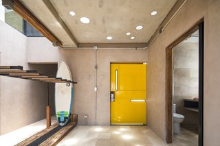 The bright yellow door adds a playful touch to a concrete abode. There is ample storage for surf gear throughout the dwelling, creating a connection between inside and out.