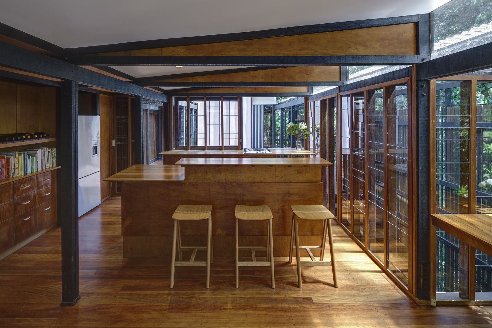 At the center of the house, on the upper level, is a kitchen and dining area fitted with glazed walls thst can be opened to connect with the outdoor decks, and green landscape.