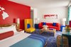 Modern home with Bedroom, Night Stands, Table Lighting, Lamps, Chair, Carpet Floor, Wall Lighting, Bed, and Dresser. Each guest room follows a color scheme of contrasting primary colors. Photo 12 of Shoreline Hotel Waikiki