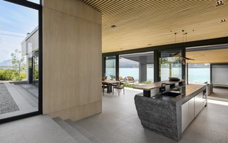 The corridor ends at the kitchen with a solid granite island that looks out over an open-plan dining and living area. This space features a fireplace and picture window that is set within a large concrete hearth wall. 