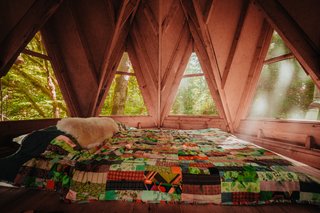 An octagonal cabin boasts a lofted sleeping area with views of the forest outside.