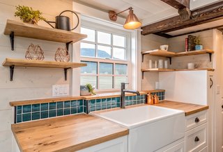 The kitchen is fitted with oak countertops, a farm sink, white cabinetry, a green tile backsplash, an LG 28-inch fridge, a 24-inch kitchen stove by Unique Off-grid Appliances, and a range hood. 