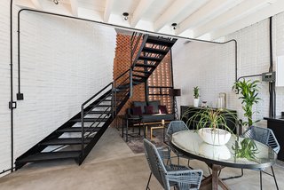 A sculptural metal staircase leads up from the open common area to the mezzanine bedroom.