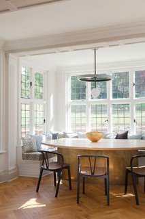 The dining area is comprised of plush banquet seating set along the walls of a spacious, window-wrapped alcove, as well as a bespoke brass-and-oak dining table designed by the duo and manufactured by British design brand Novocastrian. The contemporary chairs are by Ercol.