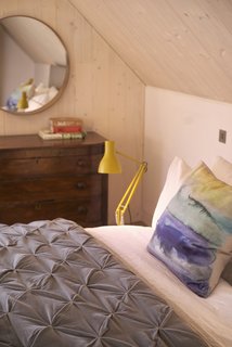 A cozy lofted bedroom with an antique dresser and an Angelpoise Type 75 lamp.