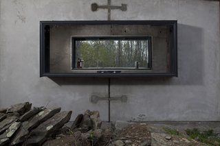 The concrete cabin has a steel chimney and window frames.