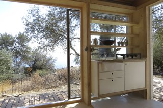 Solid Timber door with hanging pegs to hold the sink cover/chopping board – designed and built by Echo Living. The floating kitchenette unit with drawers and cupboard has a set-in Butler ceramic kitchen sink, and integral compact 12v fridge. The open shelves were designed and built by Echo Living. White Ceramic 300 x 300mm floor tiles from a range at Afoi Kathekklaki, Rethymno, Crete.