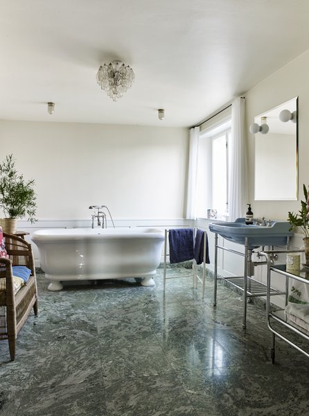 Green Swedish marble floors add a luxe touch to the bathroom. The small, vintage polydrone chandelier in clear glass is from The Apartment.