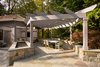A new flagstone patio protects guests from the sun while relaxing or dining. A large pergola is bordered by a gas fire pit for warmth and ambient lighting. Pendant lights hang from the pergola for additional light after sunset. Photo of Outdoor Kitchen and Patio modern home