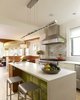 Modern home with Bench, Sofa, Chair, Media Cabinet, Bookcase, Pendant Lighting, Light Hardwood Floor, Engineered Quartz Counter, White Cabinet, Wood Cabinet, Mosaic Tile Backsplashe, Range Hood, Kitchen, Refrigerator, Range, Dishwasher, Wine Cooler, Undermount Sink, and Drop In Sink. In the kitchen, accents of vibrant green, golden yellow and earthy brown reference shades seen in the garden beyond. Photo 5 of Urban Garden House