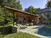 Modern home with Slope, Stone Patio, Porch, Deck, Trees, Hardscapes, Walkways, Back Yard, Shrubs, Swimming Pools, Tubs, Shower, Large Pools, Tubs, Shower, Standard Construction Pools, Tubs, Shower, Pavers Patio, Porch, Deck, Vertical Fences, Wall, Sofa, Recliner, Standard Layout Fireplace, Wood Burning Fireplace, Ceiling Lighting, and Outdoor. The pool house footprint is shaped by unique site conditions. Photo 3 of Modern Pool House