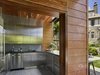 Modern home with Slope, Trees, Walkways, Hardscapes, Stone Patio, Porch, Deck, Back Yard, Shrubs, Pavers Patio, Porch, Deck, Vertical Fences, Wall, Granite Counter, Dishwasher, Metal Cabinet, Limestone Floor, Refrigerator, Ceramic Tile Backsplashe, Beverage Center, Ice Maker, Undermount Sink, and Kitchen. Outdoor kitchen Photo 4 of Modern Pool House