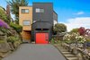 The front of the Monolith is framed by granite and basalt rock walls and features clear cedar siding, Sherwin Williams Tricorn Black painted wood siding, and Sherwin Williams Tomato red custom painted Clopay garage door. Photo of The Monolith modern home