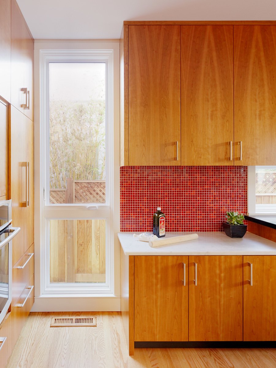 In this California home, a red mosaic tiled backsplash balances the lower white marble counter.