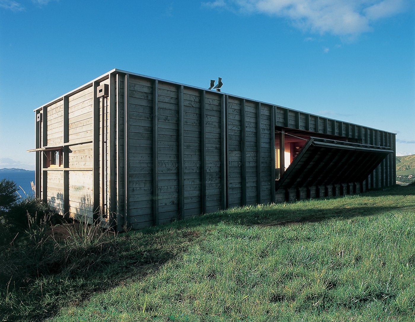 Located on New Zealand’s North Island along the Coromandel Peninsula, this timber-clad shipping container house by Crosson Clarke Carnachan Architects captures the simplicity of living with nature. An open-plan layout extends the interior toward the surrounding landscape and ocean, while a built-in mechanism reveals a drop-down deck on one side of the unique holiday home.