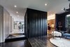 Modern home with Living Room, Chair, End Tables, Pendant Lighting, Rug Floor, Recessed Lighting, and Dark Hardwood Floor. Black walls were used to create contrast, and the black board-and-batten box is the powder room that separates the kitchen and the hallway with a glimpse of the living area beyond. The kitchen, living, and dining areas extend out to the exterior deck. Photo 8 of Mullet House