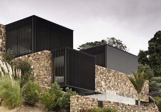 The rear of the house has a pool and patio whose smooth concrete contrasts with the varied texture and color of the stone walls.